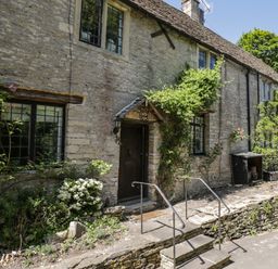 A stone cottage facade with climbing plants and flowers by the entrance steps at Fox Den Cottage in Castle Combe