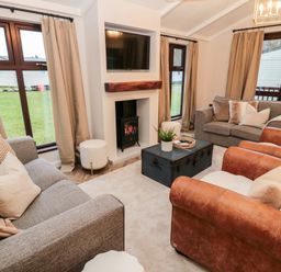 A living room with sofas armchairs a fireplace and a television at The Treeline in Swarland near Felton