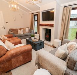 A living room with two brown armchairs two grey sofas a television above a fireplace and windows with beige curtains at The Treeline Swarland near Felton