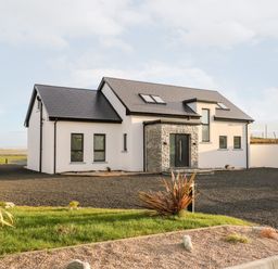 A modern house with white walls, black roof, and stone entrance surrounded by gravel driveway and plants at The Beachhouse in Meenlaragh near Gortahork, County Donegal