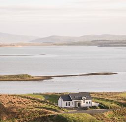 A house near a large body of water with hills in the background at The Beachhouse Meenlaragh near Gortahork County Donegal