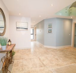 A hallway with a bicycle-shaped table holding a plant and lantern a round wall mirror paintings on walls and glass staircase railing at The Beachhouse in Meenlaragh near Gortahork County Donegal