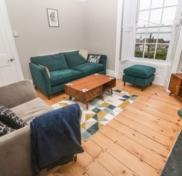A living room with green and grey sofas a wooden coffee table a patterned rug and a television on a wooden stand at Belmont in Newlyn