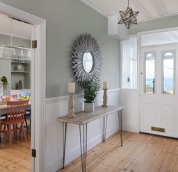An entryway with a wooden console table holding two candles and a plant and a round decorative mirror on the wall at Belmont in Newlyn