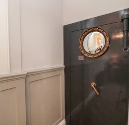 A close up of a black metal vault door with a round window and handle in a hallway at The Vault House in Bellingham