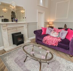 A living room with a purple sofa pink cushions a glass coffee table and a fireplace at The Vault House in Bellingham
