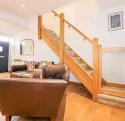 A living room with brown leather chairs a blue front door and a wooden staircase with glass panels at Min Y Mor - Morfa Nefyn