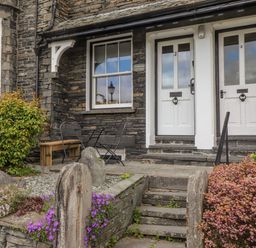 Front entrance of a cottage with two white doors stone steps stone walls and flower bushes at Primrose Cottage Ambleside