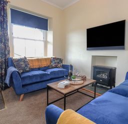 A living room with blue sofas a wooden coffee table a wall mounted tv and a small stove at Primrose Cottage in Ambleside
