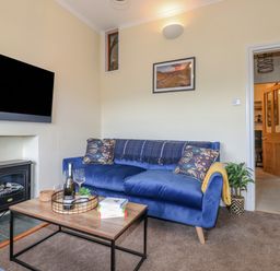 A living room with a blue sofa a wooden coffee table with books and drinks and a wall-mounted TV at Primrose Cottage in Ambleside