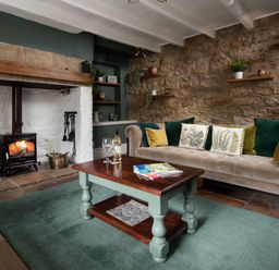 A living room with a fireplace a beige sofa with cushions a wooden coffee table and stone walls at Owl Cottage in Morpeth
