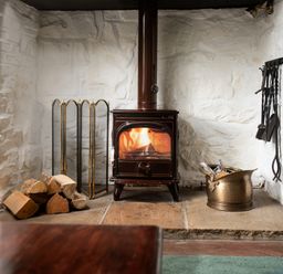 A wood-burning stove with firewood and fireplace tools in a white brick fireplace at Owl Cottage in Morpeth