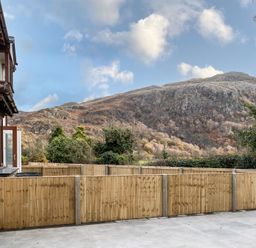 A view of a mountainous landscape behind a wooden fence from a paved patio at Hebog in Beddgelert