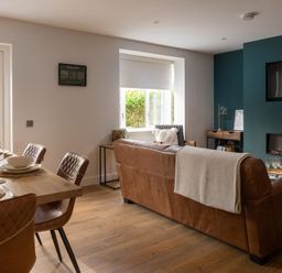 A living room with a brown leather sofa a wooden dining table with brown chairs and a wall mounted television at Hebog in Beddgelert
