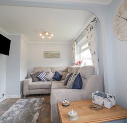 A living room with a gray sofa and cushions a wall-mounted tv an electric fireplace and a wooden side table at Merryfield Lodge in Rosecraddoc near Liskeard