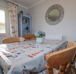 A dining room with a table covered by a patterned plastic tablecloth and wooden chairs at Merryfield Lodge in Rosecraddoc near Liskeard