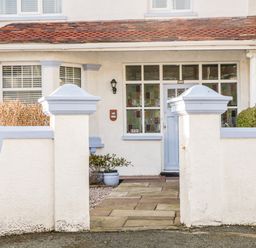 A front entrance of a house with a tiled pathway white walls and a blue door at 3 St Davids Place in Llandudno