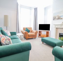 A living room with green sofas a brown armchair a television on a wooden stand and a fireplace at 24 Cadnant Park in Conwy