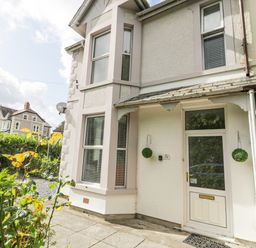 The front entrance of a white house with a door and windows surrounded by plants and neighboring houses at 24 Cadnant Park in Conwy