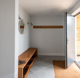 An entryway with a wooden bench with baskets underneath a round mirror and wall hooks next to an open door at The Old Coastguard Lookout in Port Isaac