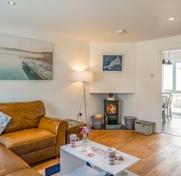 A living room with a brown leather sofa a white coffee table a wood burning stove and a floor lamp at Shrimper's Cottage in Tredrizzick near St Minver