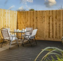 An outdoor patio area with a glass table and four chairs surrounded by wooden fencing at Shrimper's Cottage in Tredrizzick near St Minver