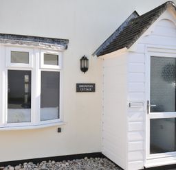 An exterior view of Shrimper's Cottage featuring a sign and windows in Tredrizzick near St Minver