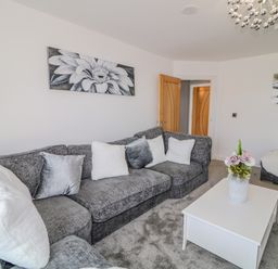 A living room with a grey sofa white cushions a white coffee table with a vase of flowers and wall art at SJs Cottage in Castlerock