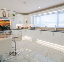 A kitchen with white cabinetry a kitchen island with stools and a large window with blinds at SJs Cottage in Castlerock
