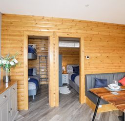A dining area with a wooden table and bench seating next to two doorways leading to bedrooms at Hilltop Lodge in Corwen