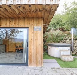 A wooden lodge exterior with sliding glass doors next to a hot tub with steps and a chimney at Hilltop Lodge in Corwen