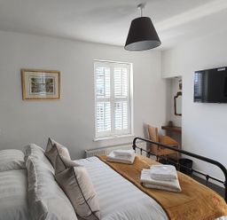 A bedroom with a double bed folded towels on it a television a chair and a window with shutters at No.37 in Beverley
