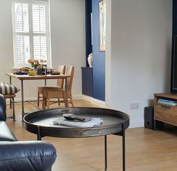A living room with a round metal coffee table a leather sofa a dining table with chairs and a television on a wooden stand at No.37 in Beverley