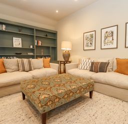 A living room with two sofas a patterned ottoman and a shelving unit at Hawthorn Barn in Northleach