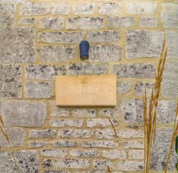 A stone wall with a sign reading Hawthorn Barn surrounded by plants at Northleach