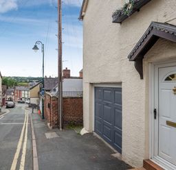 A street with a white door and garage on a beige building with houses and cars along the road at Dove Cottage in Ruthin