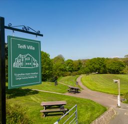 A green sign for Teifi Villa with picnic benches and a path in a grassy park area at Teifi Villa in St Dogmaels