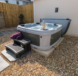An outdoor hot tub with steps and purple towels on a gravel surface with a wooden fence and stone wall in the background at Teifi Villa in St Dogmaels