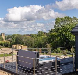 An outdoor deck area with a hot tub surrounded by metal railings and a view of trees and buildings at Foxes Den in Allerston near Thornton Dale