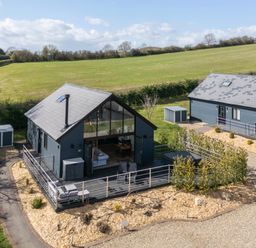Two modern single-storey houses with dark exteriors and pitched roofs with chimneys in a rural area with grassy fields at Foxes Den in Allerston near Thornton Dale