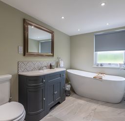 A bathroom with a toilet, sink cabinet with mirror, bathtub under a window and a towel rack at Eagles Peak in Allerton near Thornton-Le-Dale