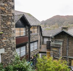 Stone buildings with multiple windows and rooftops with a background of trees and hills at Dixon Court in Ambleside