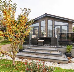 A modern wooden cabin with a deck and outdoor wicker furniture surrounded by plants and trees at Hideaway Lodge in Runswick Bay
