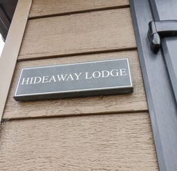 A black nameplate with white text reading Hideaway Lodge mounted on a brown wooden wall next to a black door handle at Hideaway Lodge in Runswick Bay