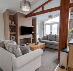 A living room with two sofas a wooden coffee table a mounted television wooden shelving and large windows at Hideaway Lodge in Runswick Bay