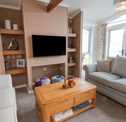 A living room with two sofas a wooden coffee table a wall-mounted TV and shelves with decorations at Hideaway Lodge in Runswick Bay