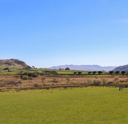 A green field with trees and hills under a clear blue sky at Hen Beudy in Porthmadog