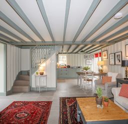 An open living and dining area with sofas rugs coffee table and stairs leading upstairs at Hen Beudy in Porthmadog