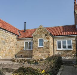 A stone cottage with red tile roof and white framed windows surrounded by a garden path and shrubs at Rose Cottage in Faceby near Swainby