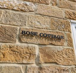 A stone wall with a sign that reads Rose Cottage next to a window at Rose Cottage Faceby near Swainby